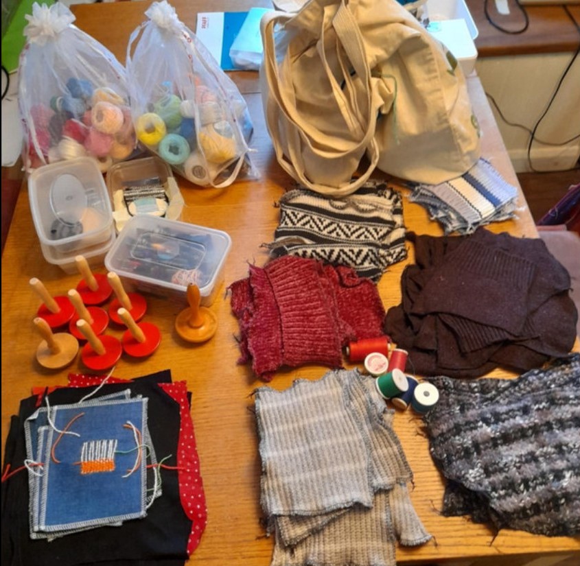 Everything needed to run a mending workshop, laid out on a table, ready to be packed. Lots of swatches of knitted fabric and lots of wool to mend them with